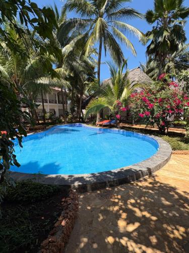 a swimming pool in front of a resort with palm trees at African Bungalows in Nungwi