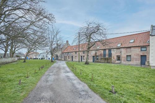 a dirt road in a field next to a building at Town Farm Cottages Beadnell by Coast & Country Stays in Beadnell
