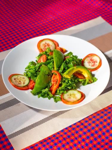 a plate of salad with tomatoes and greens on a table at Skill forest lodge in Arusha