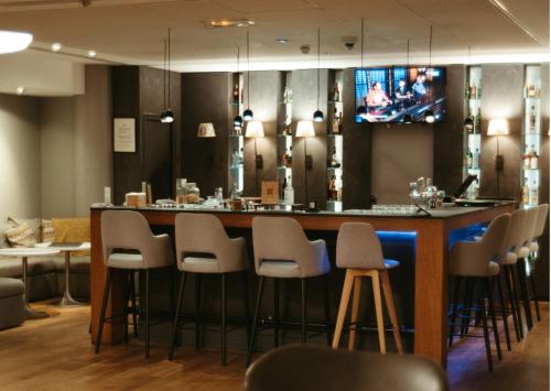 a bar with stools and a tv on the wall at Pullman Toulouse in Blagnac