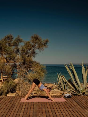 a woman doing a yoga pose on a mat near the ocean at Bikini Island & Mountain Hotel Es Trenc -Adults only- in Colonia Sant Jordi