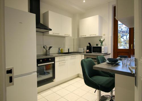 une cuisine avec des placards blancs et une table avec des chaises vertes dans l'établissement Le Shilichic - Gare, à Schiltigheim