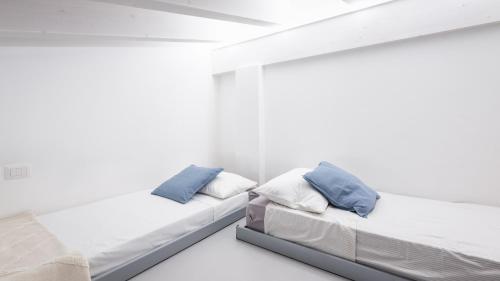 two beds in a room with white walls and blue pillows at Dimora Campo delle Mura - Charming House in Acquaviva Picena