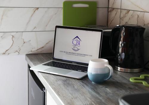 a laptop computer sitting on a counter with a coffee cup at CB Stays Contractor Hub Peterborough in Peterborough