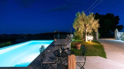 a swimming pool at night with a table and chairs at Dimora Campo delle Mura - Charming House in Acquaviva Picena