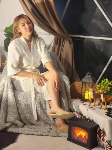 a woman sitting in a bed next to a fireplace at Geffen Khaokho in Khao Kho