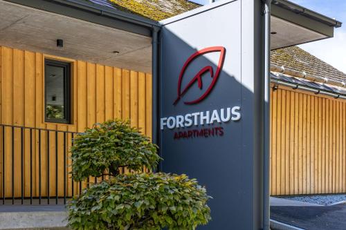 a sign in front of a building with two bushes at Forsthaus Apartments - Die Ruheoase nahe Klaffer in Klaffer am Hochficht