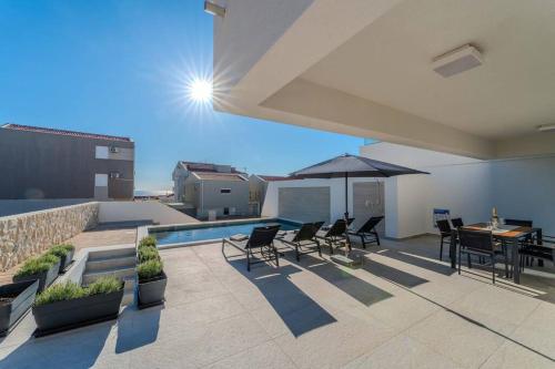 a patio with chairs and a table and an umbrella at Villa Nova Excellence 2, villa with private pool in Novalja