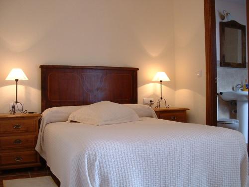 a bedroom with a bed with a white blanket and two lamps at Casa Rural Cendal in Navacarros