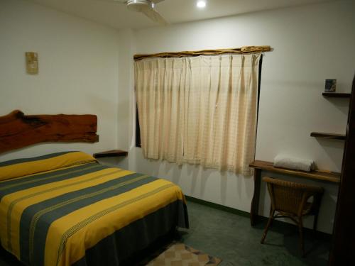 a bedroom with a bed and a window and a chair at Madre Tierra Hostal in Puerto Escondido