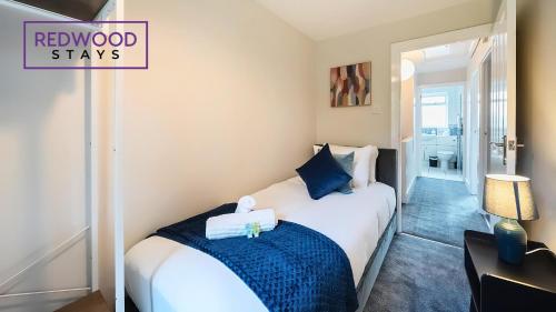 a bedroom with a white bed with a blue blanket at 3 BEDROOM SERVICED HOUSE WITH FREE PARKING FOR 2 CARS, FREE WiFi, PERFECT FOR BUSINESS STAYS, FAMILIES, RELOCATIONS, EXTENDED STAYS, AND EMERGENCY ACCOMMODATION by REDWOOD STAYS in Camberley