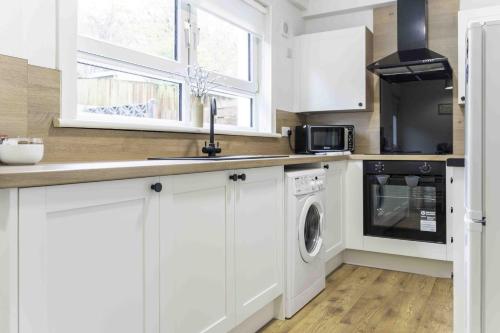 a kitchen with white cabinets and a washer and dryer at Glentarbet House in Glasgow