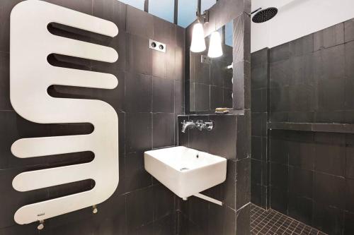 La salle de bains est pourvue d'un lavabo et d'un mur carrelé noir. dans l'établissement Spacious Vintage Duplex Flat - Gare du Nord, à Paris