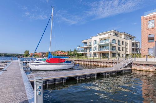 a sailboat docked at a dock next to a building at Pusteblume - Barrierefreie 5-Sterne-Ferienwohnung mit Seeblick und Sauna in Malchow
