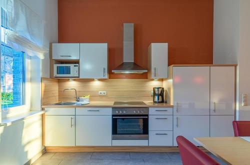 a kitchen with white appliances and an orange wall at Ferienwohnung Haubentaucher - Historische Scheune mit Seezugang im Naturpark für Familienurlaub mit Hund in Jabel