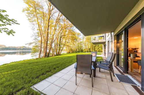 a patio with a table and chairs and a view of a lake at Lotusblume - 5 Sterne Ferienunterkunft mit möblierter Terrasse am Krakower See in Krakow am See