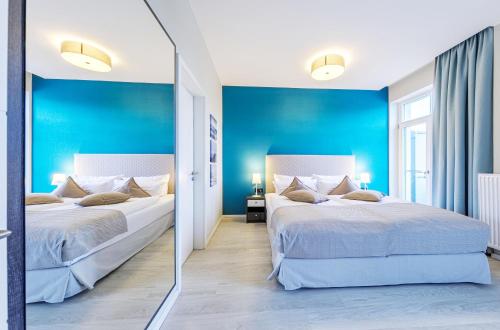 two beds in a room with blue walls and a mirror at Boddenzeit - Moderne Ferienwohnung mit Nordbalkon, Wellnessbereich und Nähe zum Ostseestrand in Wustrow