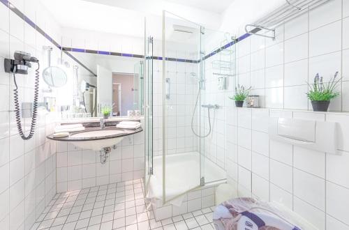 a white tiled bathroom with a shower and a sink at Kapitän Ed an der Seebrücke Zingst in Zingst