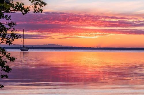 a sunset over a body of water with a sailboat at StrandLiebe am Strandbad in Malchow