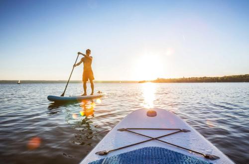 a man is standing on a paddle board in the water at Ferienwohnung Hafenglück- Ideal für Familien mit Balkon und Yachthafenblick in Waren
