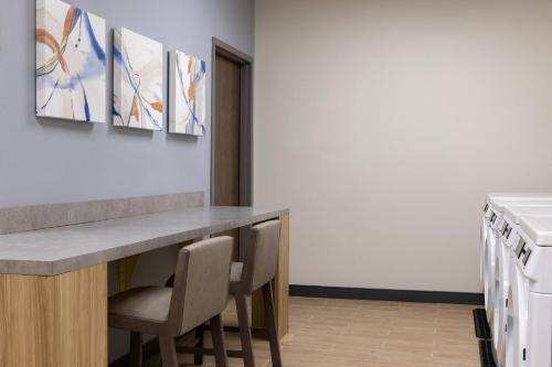 a kitchen with a counter with chairs and paintings on the wall at Candlewood Suites Middletown - Goshen by IHG in Middletown