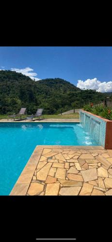 a swimming pool with blue water and mountains in the background at Pousada Vale das Araucárias in Santo Antônio do Pinhal
