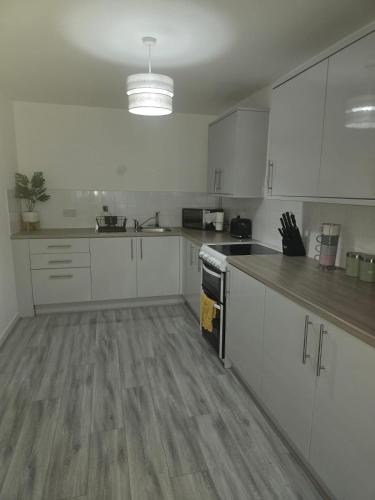 a kitchen with white cabinets and a wooden floor at New 4bedroom house near Manchester Airport in Handforth