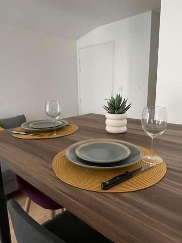 a wooden table with two plates and wine glasses at Duplex le Brooklyn en Plein centre de Mordelles in Mordelles