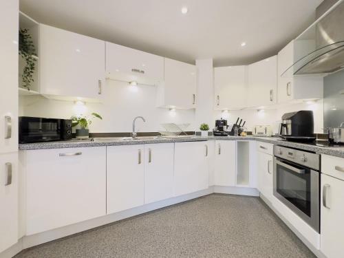 a white kitchen with white cabinets and appliances at CanaryWharf Apartments by Sleepy in London