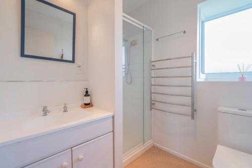 Un baño blanco con lavabo y espejo. en Across the Road to the Beach - Apartment, en Whitianga