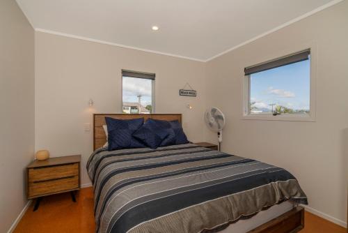 Un dormitorio con una cama y dos ventanas. en Across the Road to the Beach - Apartment, en Whitianga