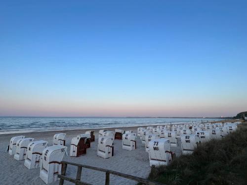 a row of white chairs on the beach at Ostseecamp Ferienhaus "StrandPerle" in Scharbeutz