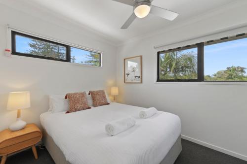 a white bedroom with a bed and two windows at Gosamara Apartments in Byron Bay