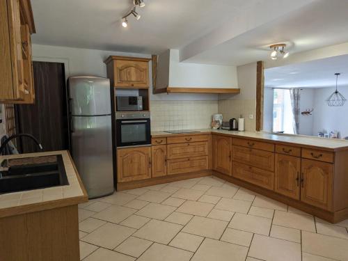 une cuisine avec des armoires en bois et un réfrigérateur en acier inoxydable dans l'établissement Charmante maison de campagne avec jardin privé, près de Paris et Orléans, idéale pour familles - FR-1-590-136, à Audeville