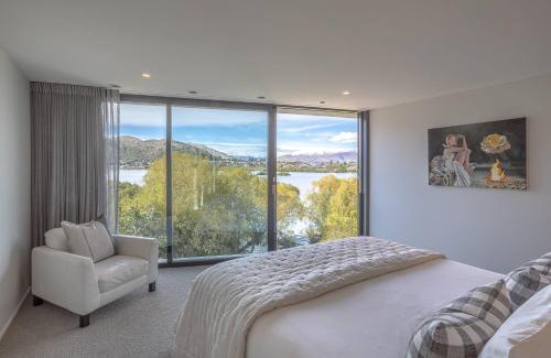 a bedroom with a bed and a chair and a large window at Willow Waters - lakeside luxury - a Relax it's Done holiday home in Frankton Wharf