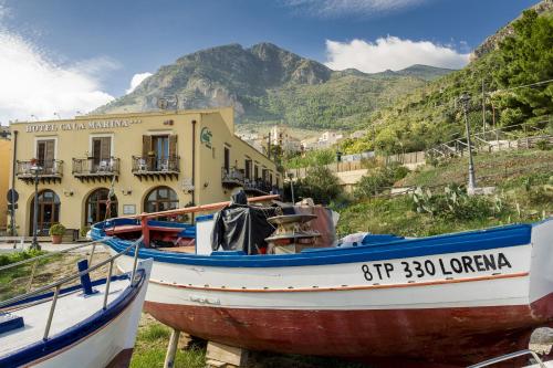 dwie łodzie siedzące na trawie przed budynkiem w obiekcie Hotel Cala Marina w mieście Castellammare del Golfo