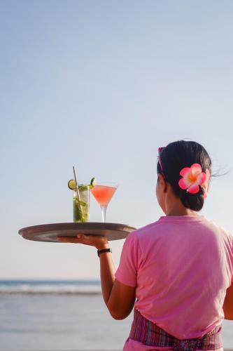 a woman holding a tray with two drinks on it at PinkCoco Gili Trawangan - Constant Surprises - for Cool Adults Only in Gili Trawangan