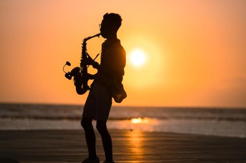 a man playing a saxophone on the beach at sunset at PinkCoco Gili Trawangan - Constant Surprises - for Cool Adults Only in Gili Trawangan
