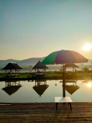 a bench with an umbrella next to a body of water at ลุงไซยเดอะแคมป์ in Ban Wang Hin Ngon