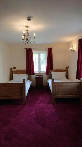 a bedroom with two beds and a window with red curtains at Great Trethew Hotel - Self Catering Lodges - Bar & Restaurant in Liskeard
