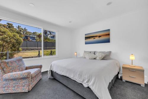 a bedroom with a bed and a chair and a window at Seascape Beach House in Pambula Beach