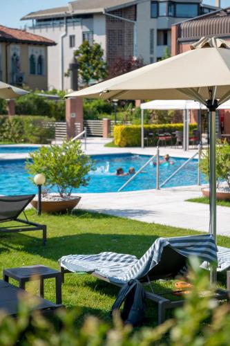a person laying in a chair under an umbrella near a swimming pool at DB Villas Le Ville del Lido Resort in Venice-Lido