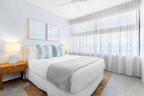 a white bedroom with a bed and a window at Bokarina Beach Apartments, an Ascend Collection Hotel in Bokarina