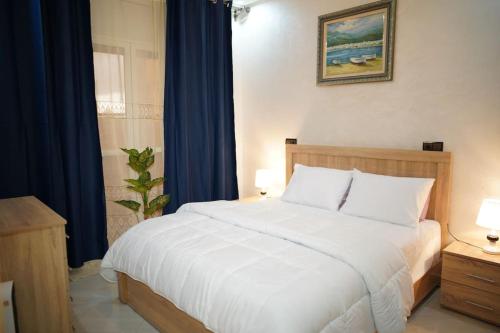 a bedroom with a large white bed with blue curtains at Spacious and Calm Apartment 100m with Balcony , Fast Fiber , Parking and IPTV in Kenitra