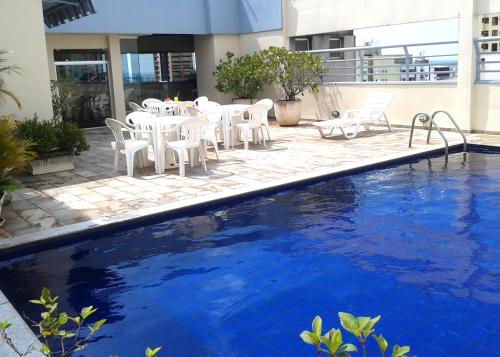 uma piscina com cadeiras brancas e uma mesa e uma piscina em Crillon Palace Hotel em Londrina