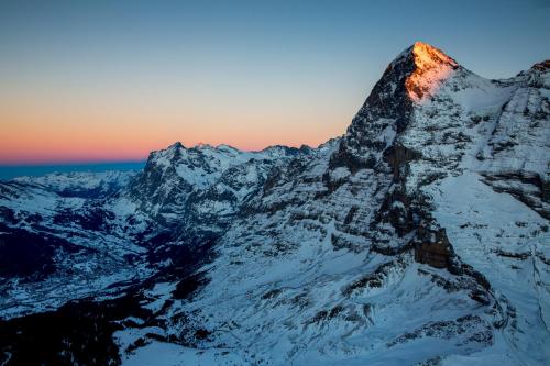 a mountain covered in snow with the sun setting on it at Hotel Kreuz & Post Grindelwald in Grindelwald