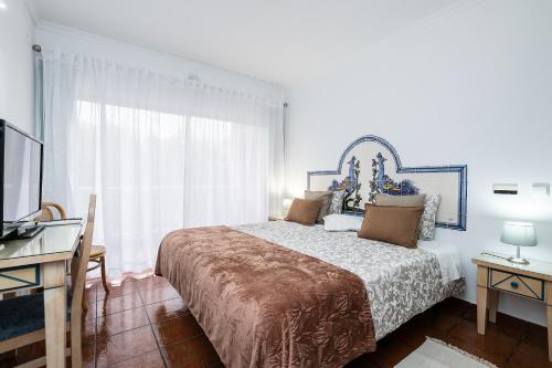 a bedroom with a bed and a desk and a window at Parque dos Reis Apartment in Monte Gordo