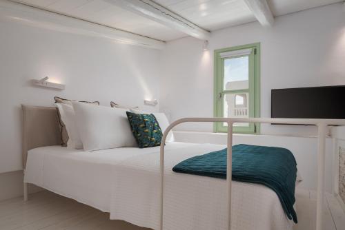 a white bedroom with a bed with a flat screen tv at Porto Sereno Andros Suites in Andros