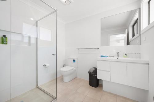 a white bathroom with a toilet and a glass shower at KozyGuru | Austral | Convenient 4 x Ensuite House in Austral