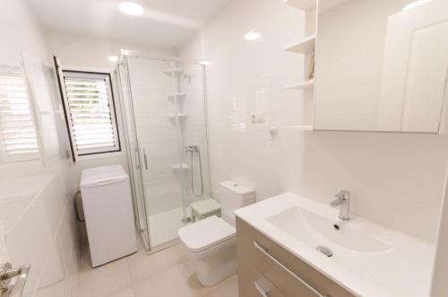 a white bathroom with a shower and a toilet and a sink at Terraced 2 bedroom beach rental in Maspalomas
